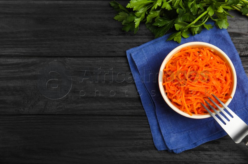 Delicious Korean carrot salad and parsley on black wooden table, flat lay. Space for text