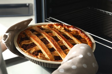 Photo of Woman taking delicious freshly baked meat pie from oven, closeup