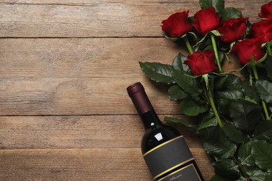 Photo of Bottle of red wine and beautiful roses on wooden table, flat lay. Space for text