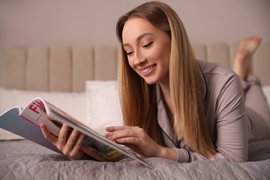 Happy woman reading magazine on bed indoors