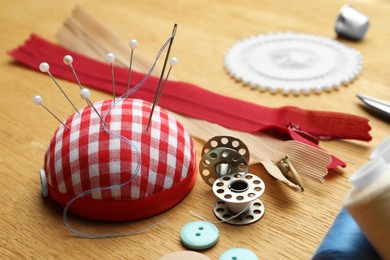 Photo of Pincushion and sewing tools on wooden table, closeup