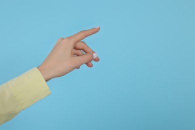 Woman pointing at something against light blue background, closeup on hand. Space for text