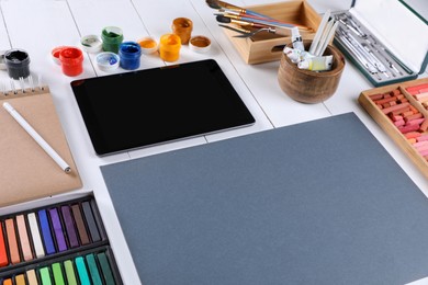 Blank sheet of paper, colorful chalk pastels, tablet and other drawing tools on white wooden table. Modern artist's workplace