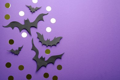 Flat lay composition with paper bats and golden confetti on purple background, space for text. Halloween decor