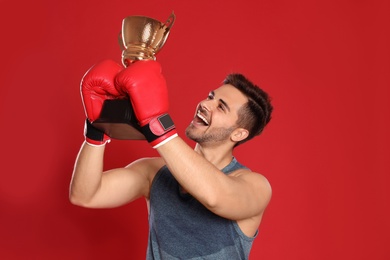 Portrait of happy young boxer with gold trophy cup on red background