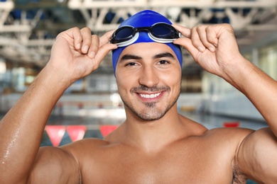 Young athletic man in cap and goggles near swimming pool