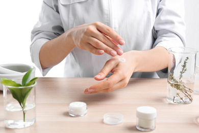 Woman applying natural cream onto hand in cosmetic laboratory, closeup