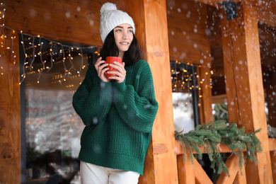 Pretty woman wearing sweater with cup near wooden terrace in winter