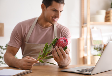 Photo of Florist with protea flower near laptop in floral store