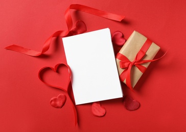 Flat lay composition with blank greeting card and gift on red background. Valentine's day celebration