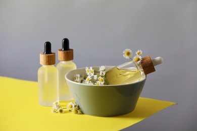 Bottles of chamomile essential oil and flowers on color background