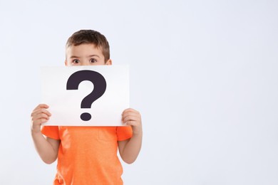 Emotional little boy holding paper with question mark on white background