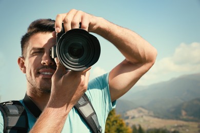 Professional photographer taking picture with modern camera in mountains, focus on lens