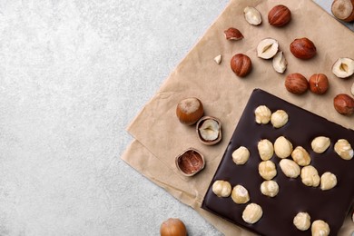 Photo of Delicious chocolate bar and hazelnuts on light grey table, flat lay. Space for text