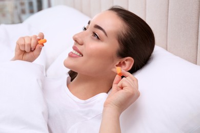 Young woman inserting foam ear plugs in bed