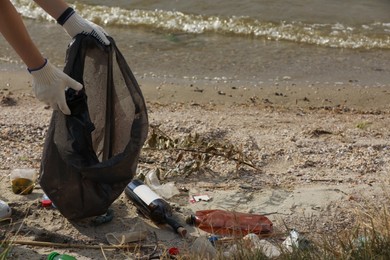 Woman in gloves with trash bag collecting garbage on beach, closeup