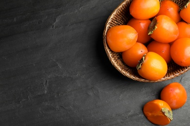 Delicious fresh persimmons on black slate table, flat lay. Space for text