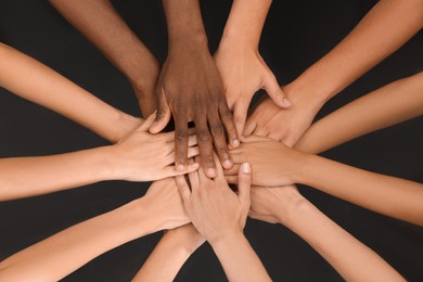 Group of multiracial people joining hands together on black background, closeup