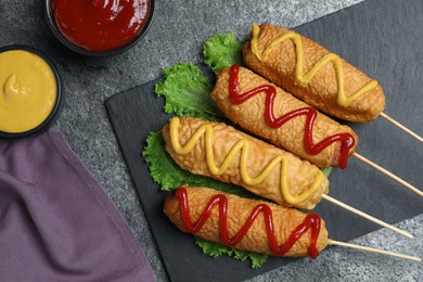 Delicious deep fried corn dogs with lettuce and sauces on grey table, flat lay