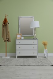 White chest of drawers with decor, coat stand and mirror in hallway. Interior design
