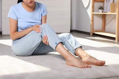 Young woman rubbing sore leg at home, closeup