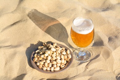 Photo of Glass of cold beer and pistachios on sandy beach, above view
