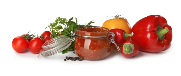Photo of Glass jar of tasty adjika and ingredients on white background