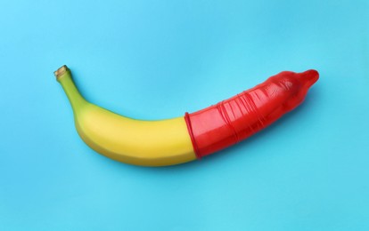 Banana with condom on light blue background, top view. Safe sex concept