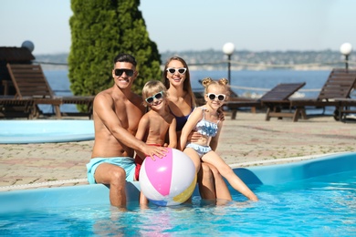 Happy family with inflatable ball at poolside on sunny summer day
