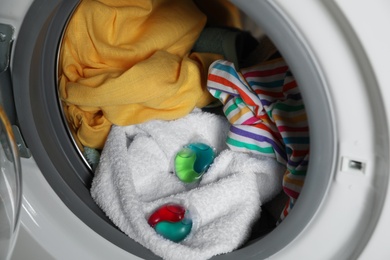 Laundry detergent capsules and clothes in washing machine drum, closeup view