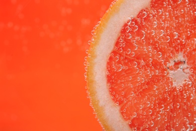 Slice of grapefruit in sparkling water on orange background, closeup with space for text. Citrus soda