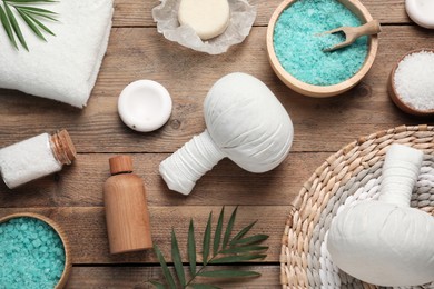 Flat lay composition with herbal massage bags and other spa products on wooden table