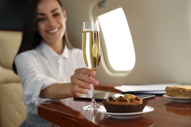 Woman with glass of champagne at table in airplane during flight, focus on hand