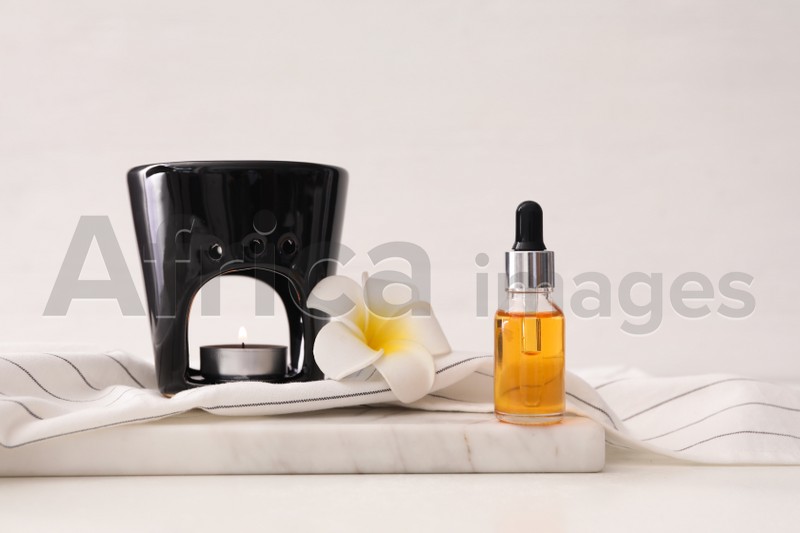 Aroma lamp, plumeria flower and bottle of essential oil on white table