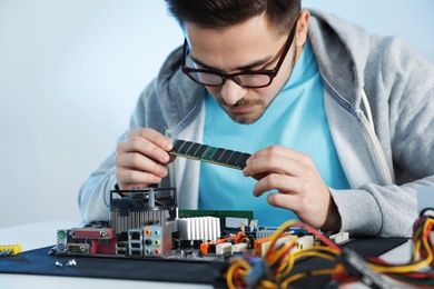 Photo of Male technician repairing motherboard at table against light background