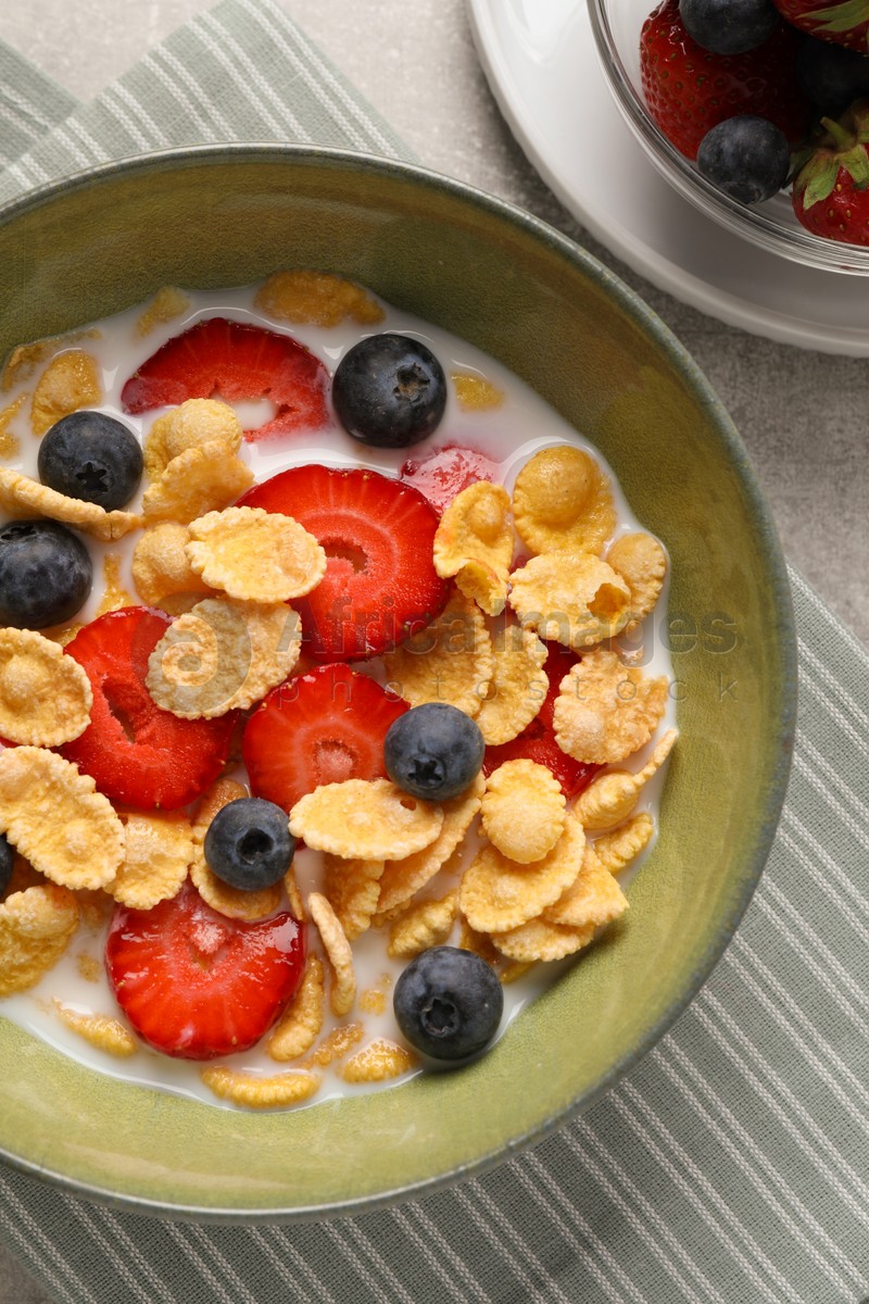 Corn flakes with berries in bowl served on grey table, flat lay