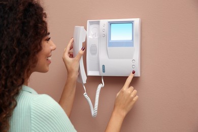 Young African-American woman pressing button on intercom panel indoors