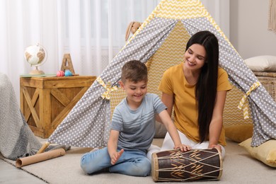 Mother and son playing on drum near toy wigwam at home