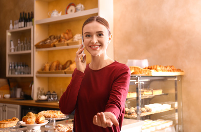 Photo of Female business owner talking on mobile phone in bakery