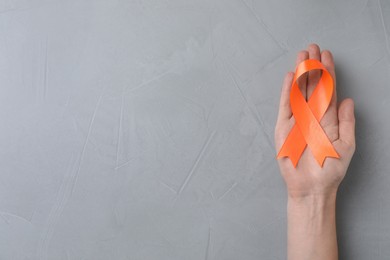 Man holding orange ribbon on light grey background, top view with space for text. Multiple sclerosis awareness