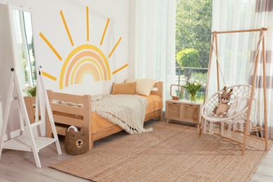 Photo of Cute child's room interior with bed, swing chair and sun art on wall