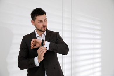 Man wearing stylish suit and cufflinks near white wall, space for text