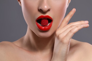Young woman with red lips makeup eating candy on grey background, closeup
