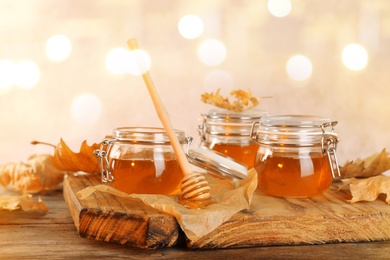 Dipper and jars with honey on table against blurred lights