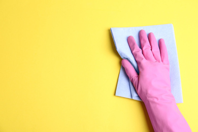 Person in rubber glove with rag on yellow background, closeup of hand. Space for text