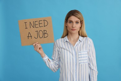 Photo of Unemployed woman holding sign with phrase I Need A job on light blue background