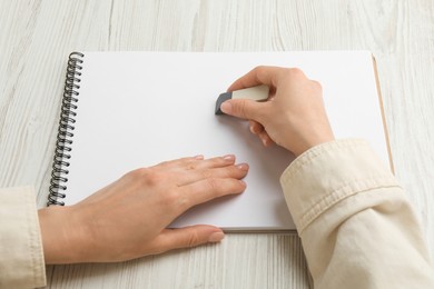 Woman erasing something in notebook at white wooden table, closeup