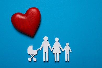 Paper family figures and red wooden heart on light blue background, flat lay. Insurance concept