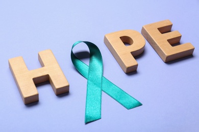 Word Hope made of wooden letters and teal awareness ribbon on lilac background. Symbol of social and medical issues