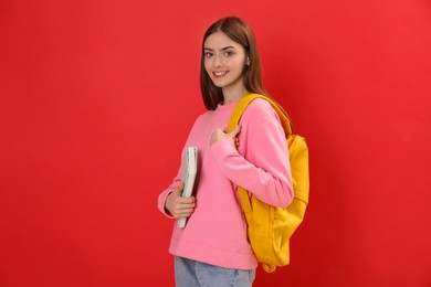 Teenage student with backpack and book on red background